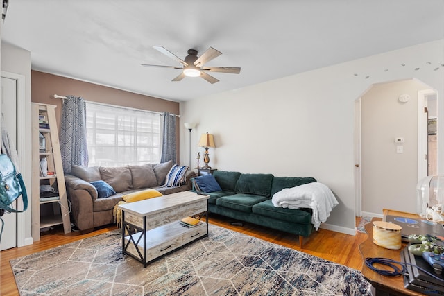 living area featuring baseboards, arched walkways, a ceiling fan, and wood finished floors