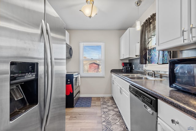 kitchen featuring white cabinets, dark countertops, a sink, stainless steel appliances, and baseboards
