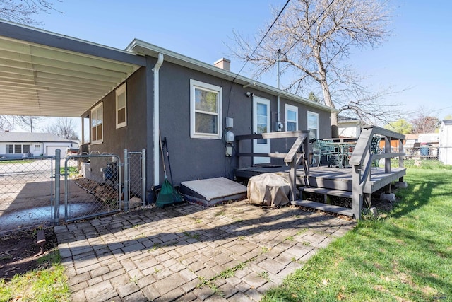 rear view of house featuring fence, a wooden deck, stucco siding, a gate, and a carport