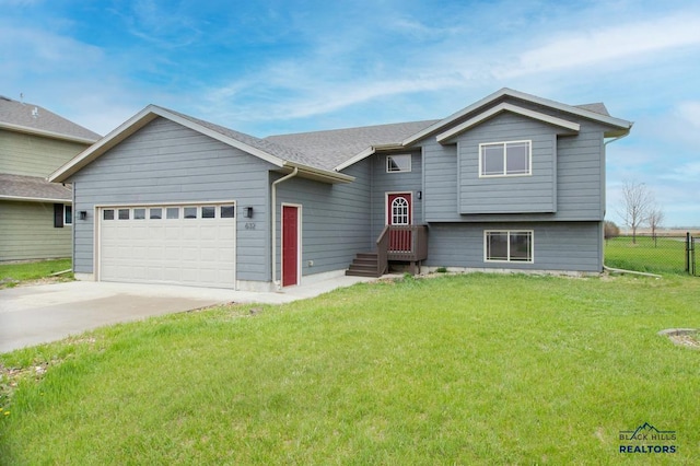 bi-level home with an attached garage, fence, driveway, and a front lawn