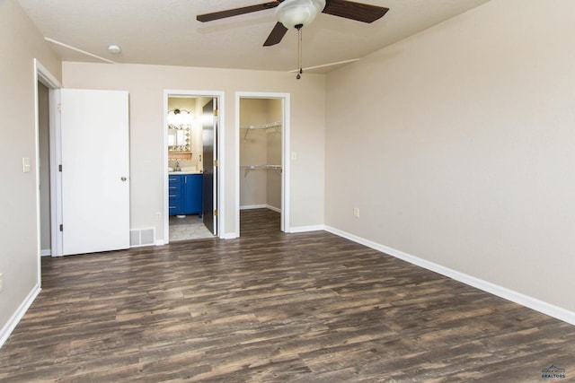 unfurnished bedroom with visible vents, baseboards, dark wood-type flooring, and a walk in closet
