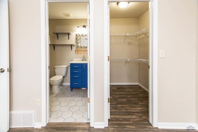 bathroom featuring visible vents, vanity, wood finished floors, toilet, and a walk in closet