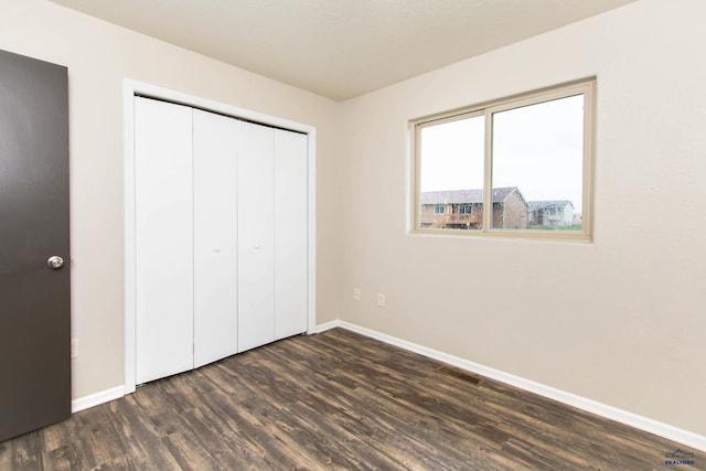 unfurnished bedroom featuring a closet, baseboards, visible vents, and dark wood-type flooring
