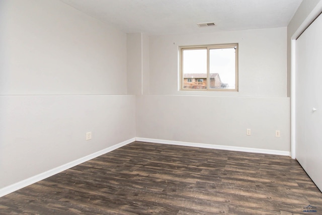 spare room with baseboards, dark wood-type flooring, and visible vents