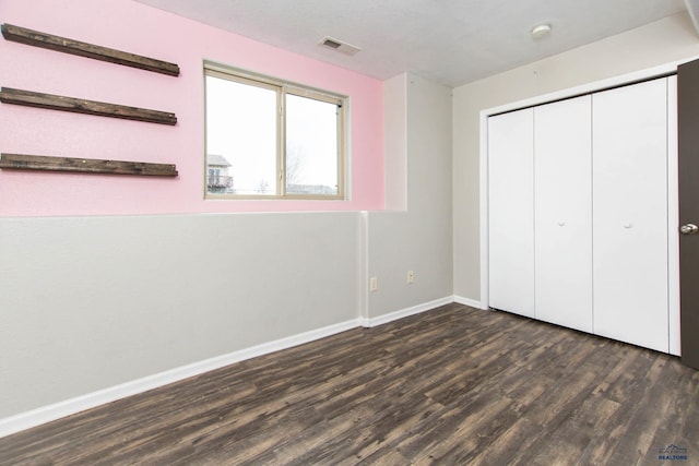 unfurnished bedroom featuring a closet, baseboards, visible vents, and dark wood-type flooring