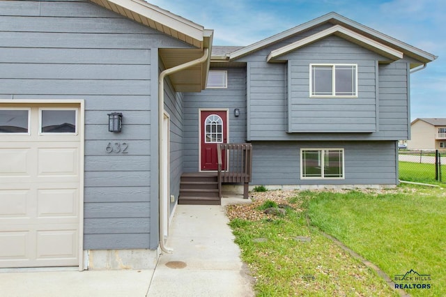bi-level home featuring an attached garage, fence, and a front lawn