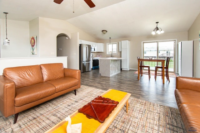living area featuring arched walkways, dark wood finished floors, ceiling fan with notable chandelier, and vaulted ceiling