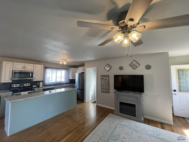 kitchen with a kitchen island, dark wood-style flooring, a sink, baseboards, and stainless steel appliances