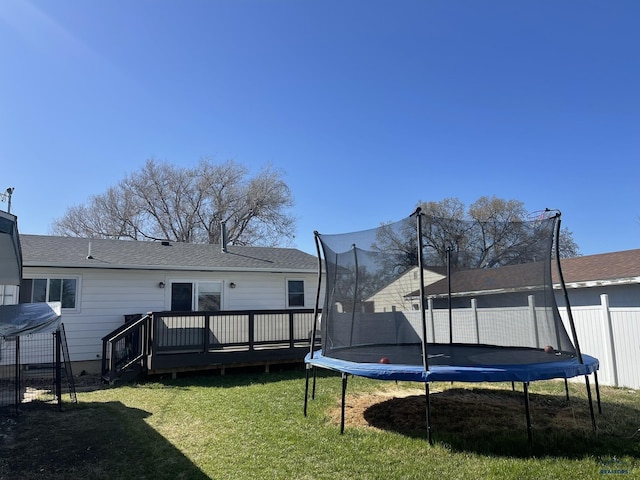 rear view of property with a yard, fence, a wooden deck, and a trampoline