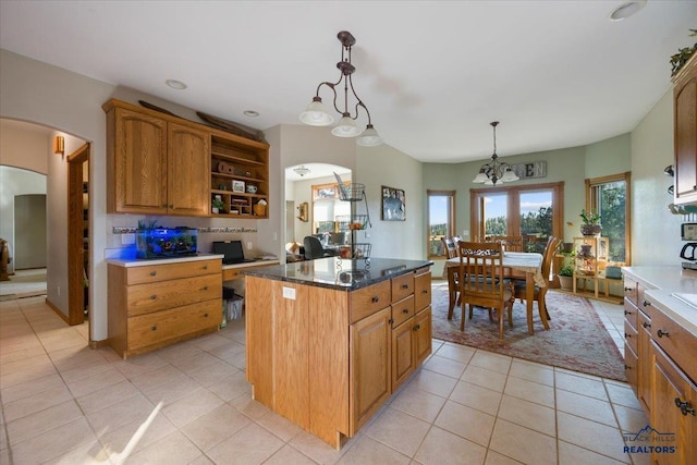 kitchen with open shelves, brown cabinets, arched walkways, light tile patterned floors, and decorative light fixtures