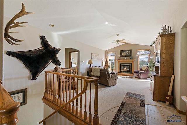 living area with ceiling fan, light colored carpet, arched walkways, lofted ceiling, and a glass covered fireplace