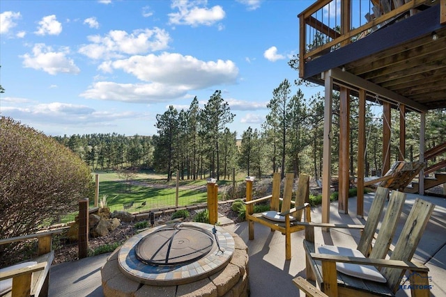 view of patio / terrace featuring a view of trees, a wooden deck, stairs, and an outdoor fire pit
