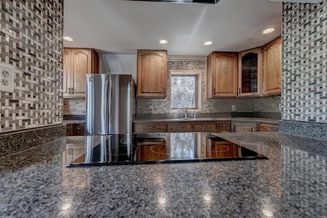 kitchen featuring tasteful backsplash, freestanding refrigerator, black electric stovetop, glass insert cabinets, and recessed lighting