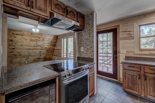 kitchen featuring plenty of natural light, wood walls, under cabinet range hood, and stainless steel electric range oven