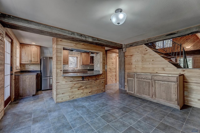 kitchen with freestanding refrigerator, wood walls, dark countertops, a sink, and backsplash