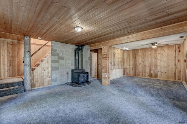 unfurnished living room with wooden walls, carpet flooring, a wood stove, stairs, and wooden ceiling