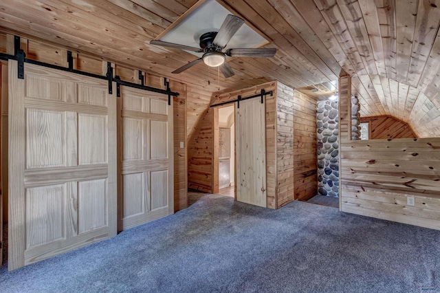 unfurnished bedroom with wooden walls, carpet flooring, a barn door, wooden ceiling, and vaulted ceiling