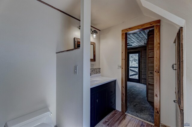 half bath with toilet, vaulted ceiling, wood finished floors, and vanity