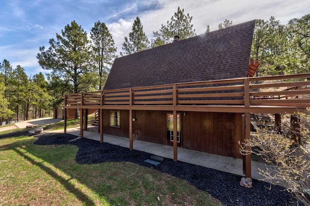 rear view of property featuring a patio, roof with shingles, a lawn, and a deck