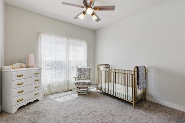 carpeted bedroom with baseboards, a crib, and ceiling fan