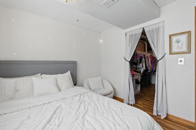 bedroom featuring visible vents, a closet, wood finished floors, baseboards, and a spacious closet