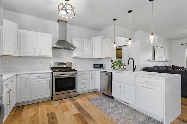 kitchen with wall chimney exhaust hood, stainless steel appliances, open floor plan, light wood-type flooring, and backsplash