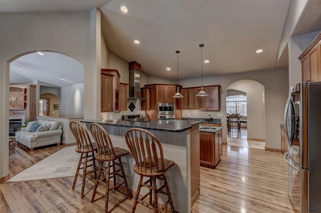 6642 Carnoustie Ct, Rapid City, SD 57702 - kitchen featuring brown cabinetry, stainless steel appliances, wall chimney range hood, a breakfast bar area, and arched walkways