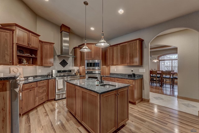 6642 Carnoustie Ct, Rapid City, SD 57702 - kitchen featuring a sink, wall chimney exhaust hood, arched walkways, stainless steel appliances, and a kitchen island with sink