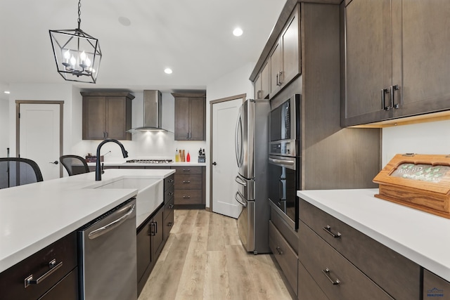 kitchen with light wood-type flooring, light countertops, appliances with stainless steel finishes, and wall chimney exhaust hood