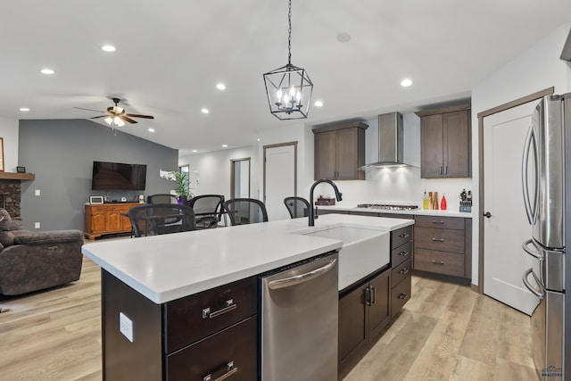 kitchen with a sink, wall chimney range hood, open floor plan, light countertops, and appliances with stainless steel finishes
