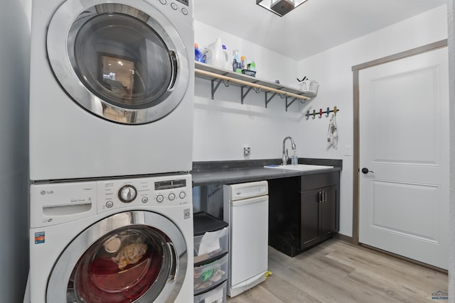 washroom featuring a sink, stacked washer and dryer, indoor wet bar, light wood-style floors, and cabinet space
