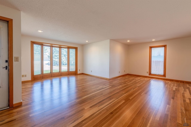 unfurnished living room with a textured ceiling, baseboards, light wood-type flooring, and recessed lighting