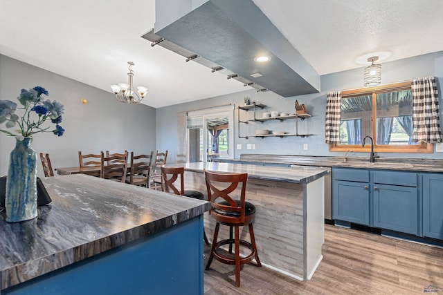 kitchen featuring a sink, blue cabinetry, a chandelier, light wood-style flooring, and a kitchen bar