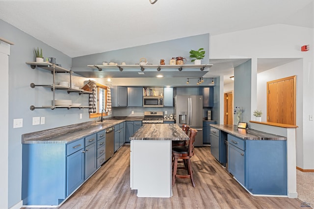kitchen featuring stainless steel appliances, open shelves, a breakfast bar, vaulted ceiling, and blue cabinets