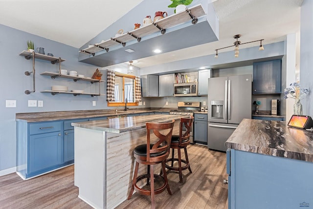 kitchen featuring appliances with stainless steel finishes, open shelves, light wood finished floors, a kitchen breakfast bar, and lofted ceiling