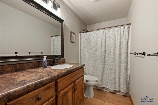 full bathroom featuring wood finished floors, vanity, toilet, a textured wall, and a textured ceiling
