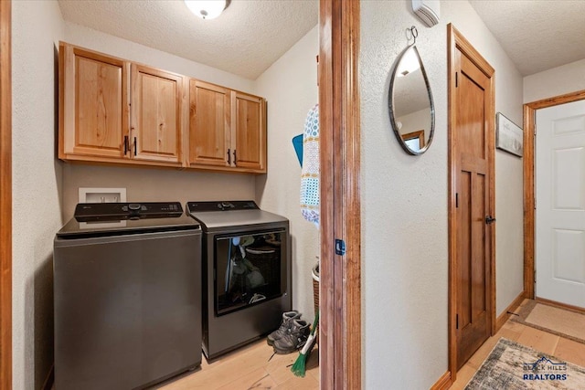 clothes washing area with cabinet space, washing machine and clothes dryer, light wood-type flooring, and a textured ceiling