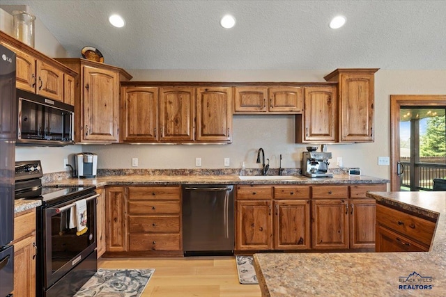 kitchen with stainless steel appliances, a sink, a textured ceiling, light wood-style floors, and brown cabinetry