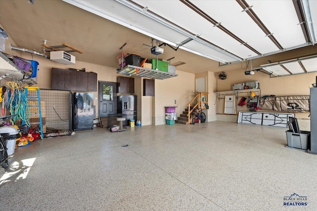 garage with stainless steel refrigerator with ice dispenser and a garage door opener