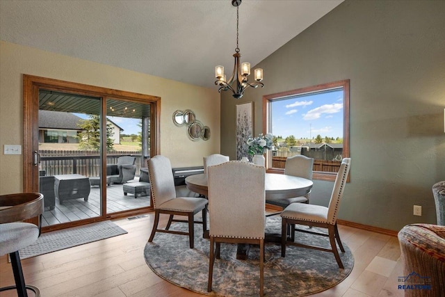 dining space with a chandelier, light wood-style floors, baseboards, and high vaulted ceiling