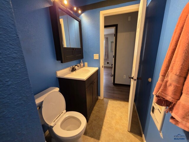 half bathroom with toilet, vanity, and a textured wall