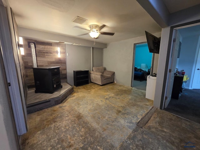 living room featuring a wood stove, a ceiling fan, and unfinished concrete floors