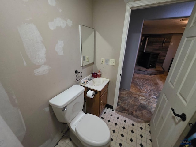 half bathroom featuring vanity, toilet, a wood stove, and tile patterned floors