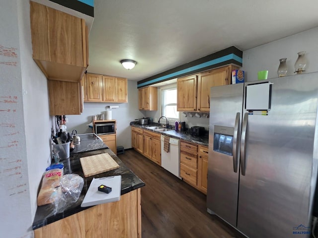 kitchen with appliances with stainless steel finishes, a sink, dark wood finished floors, and dark countertops
