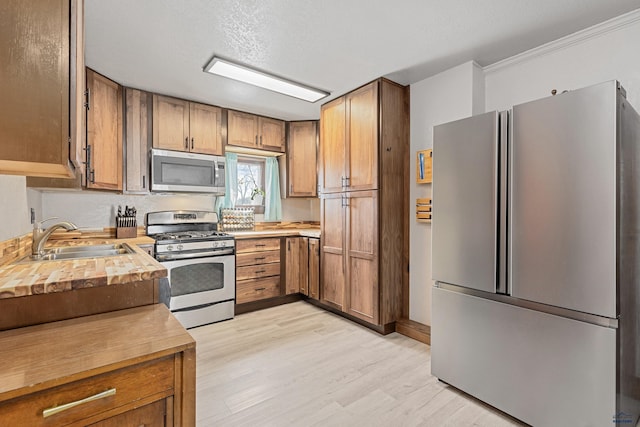 819 Sly St, Sturgis, SD 57785 - kitchen featuring stainless steel appliances, a sink, light wood-style flooring, brown cabinets, and crown molding