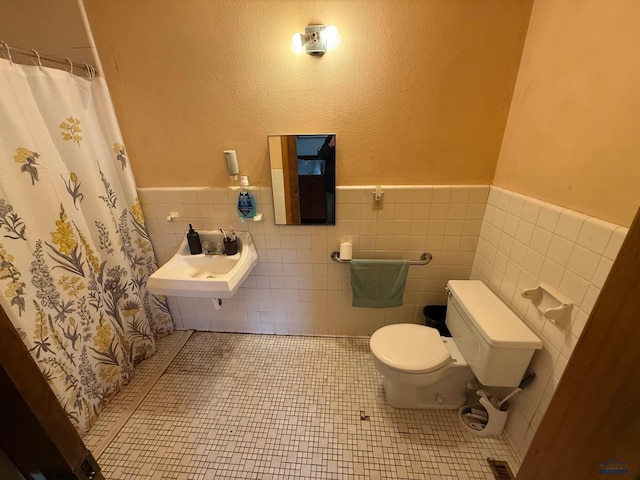bathroom with toilet, a wainscoted wall, tile walls, pet washing area, and tile patterned flooring