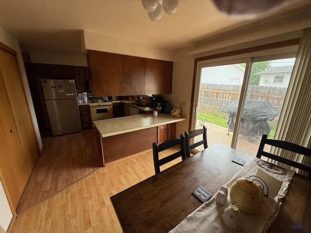 kitchen featuring freestanding refrigerator, white range with gas cooktop, a peninsula, wood finished floors, and light countertops
