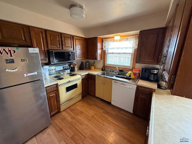 kitchen featuring white appliances, light countertops, a sink, and light wood-style floors