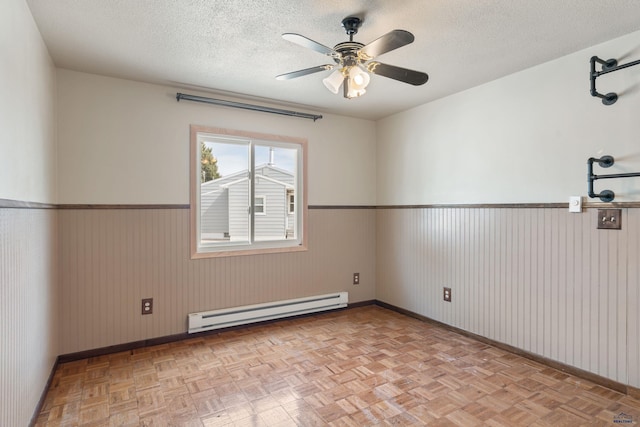 2030 12th Ave, Belle Fourche, SD 57717 - unfurnished room with a baseboard heating unit, a wainscoted wall, baseboards, a ceiling fan, and a textured ceiling