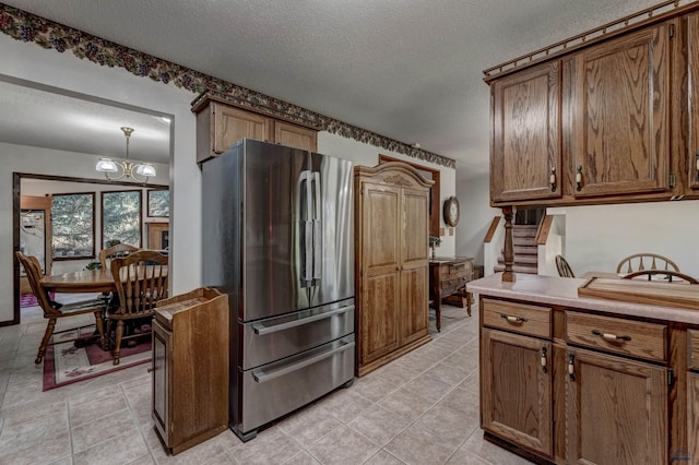 4240 Foothill Dr, Rapid City, SD 57702 - kitchen featuring freestanding refrigerator, a textured ceiling, light tile patterned flooring, brown cabinets, and a chandelier